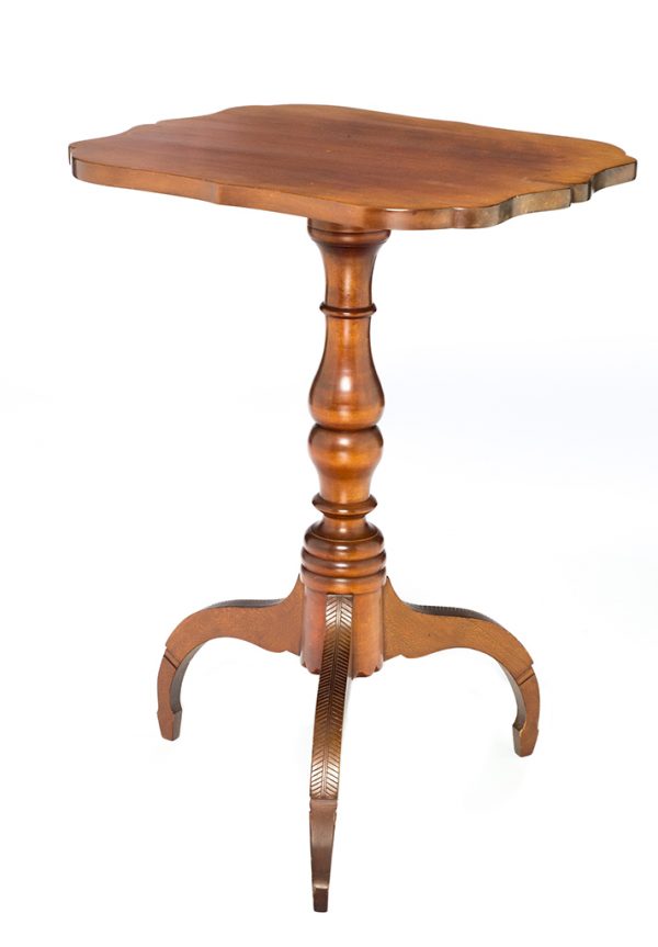 A cherry wood top and base. The top has a curved edge and a turned vertical column. The three spider legs have a chevron design carved on their top surface, spade feet.
