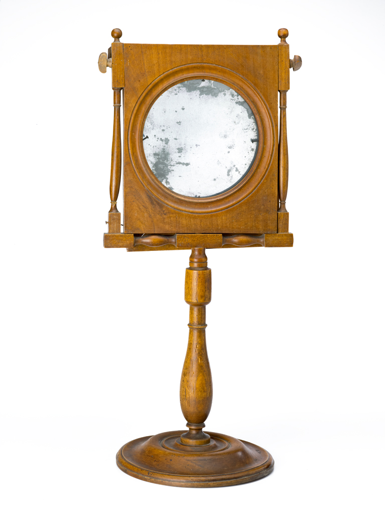 A  freestanding shaving mirror with a disk base, turned post, and rectangular two-part
frame. A magnifying glass is backed by a slivered glass. These are on hinges at the top so that the glass can be used separate from the magnifier.
