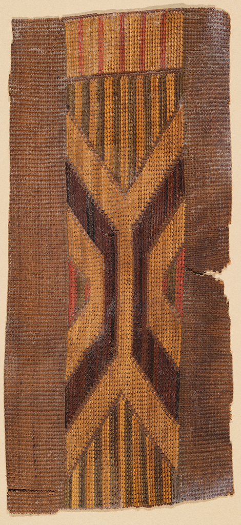 A fragment of a woven (mat?). The natural fibers are brown, tan/yellow, and orange/red.