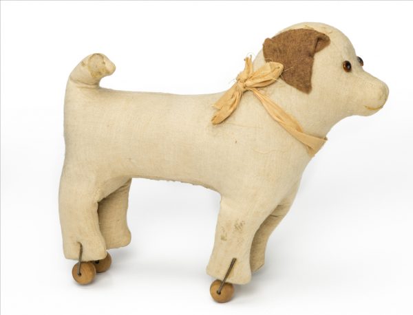 A child's pull toy depicting a standing dog. The dog is white with brown ears, casters on his feet.