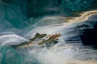 A hand rises from what appears to be a combination of water and tulle fabric. the hand is reflected above.