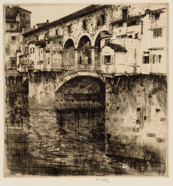 A scene in Florence of the Ponte Vecchio. The view is from the bank looking over the water to the bridge with old shops.