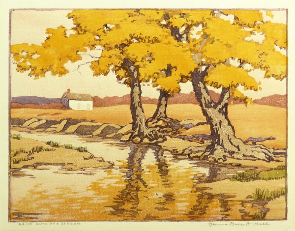 Fall colored trees stand beside a lake which they reflect inches In the distance, there is a small house and mountains.