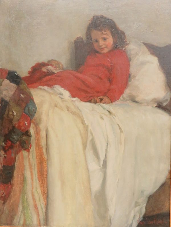 A young girl in red sleeping clothes, sits on a bed of white sheets/pillows. She smiles and holds her toes. A multi-colored comforter hangs on the toe board.