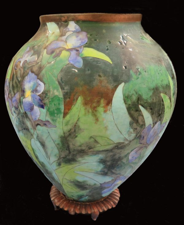 A large vase with cloisonnй exterior in green, blue and yellow depicting irises. The vase has a decorative wood stand. The rim is of copper