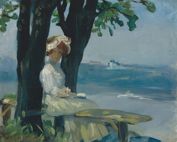 A woman in long dress and hat sits at a backless bench, reading. Trees are behind and to her left, the ocean can be seen in the distance.