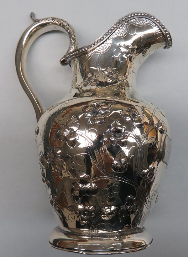 A classic pitcher shape made of hammered silver repussй. The arched handle has thumb guide.  The out rim of the pouring spout has decorative rope of tiny balls, and the body has floral shapes.