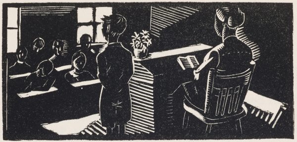 Classroom of children with teacher standing and school mistress in front of the class, sitting and reading a book.