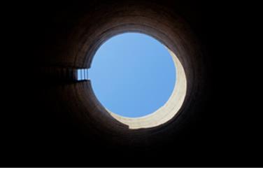 A view looking up to the sky, from inside a tall, cylindrical, structure commonly called tower silos.