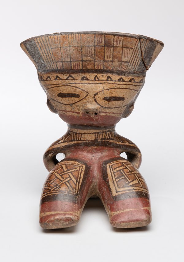 Seated figure with legs outstretches. Figure wears geometric designs on clothing and headdress.