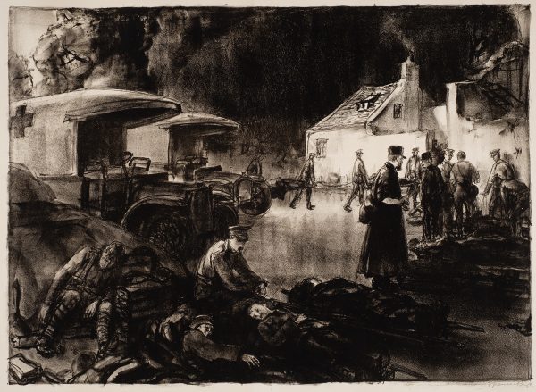 A row of injured men on litters, are being tended to by men in uniform. Trucks are to the left, and brightly lit buildings are to the right.