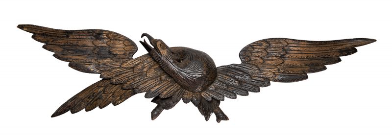 A carved eagle with outstretched wings and the head curved around looking up with open beak.