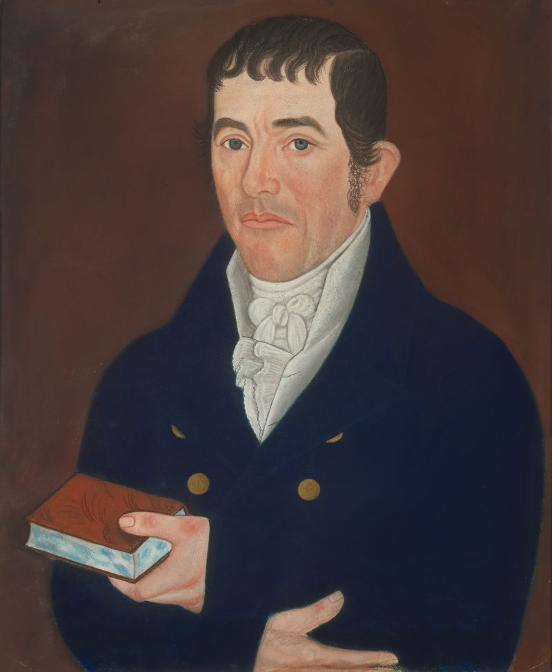 A portrait of a man wearing a blue coat. He is holding a book.