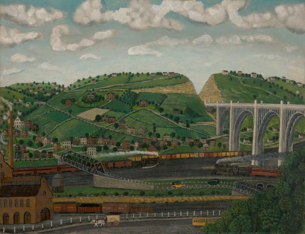 An industrial landscape including a land bridge over railroads. There are hills and homes in the distance.