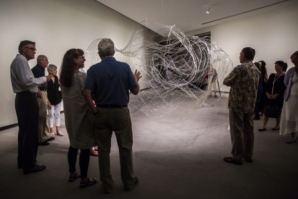 Interior image of adults in a gallery looking at a glass art installation