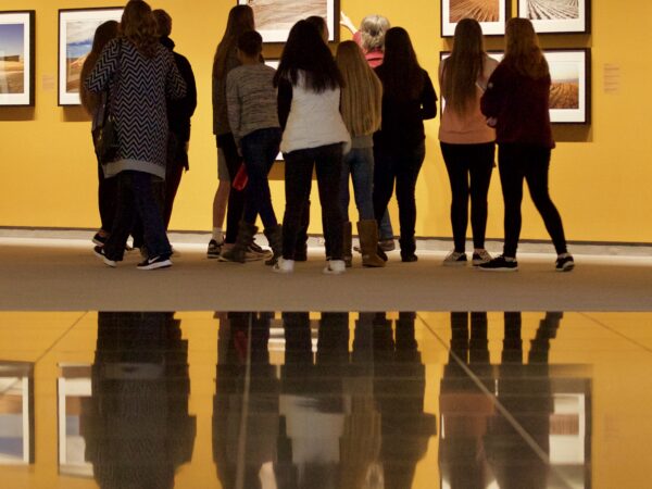 Photo of a half-dozen high school students with their backs to the camera looking at photography of Kansas on the wall