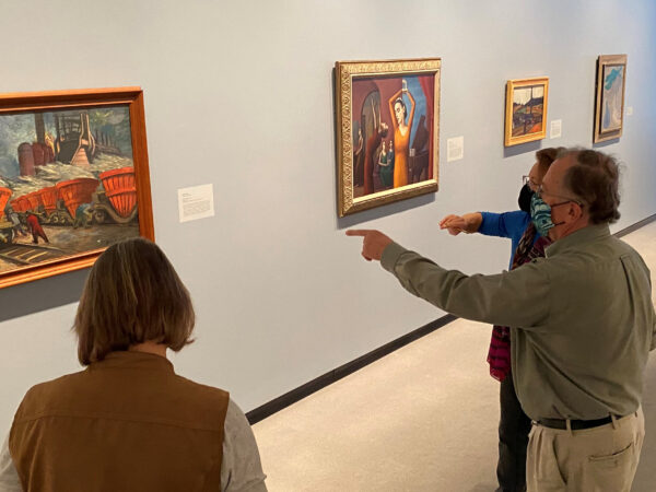 Three adults in the gallery, two pointing at a painting.