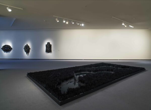 Gallery image of black glass installation. Large rectangle of glass on the floor with three sculptures on the wall in the background
