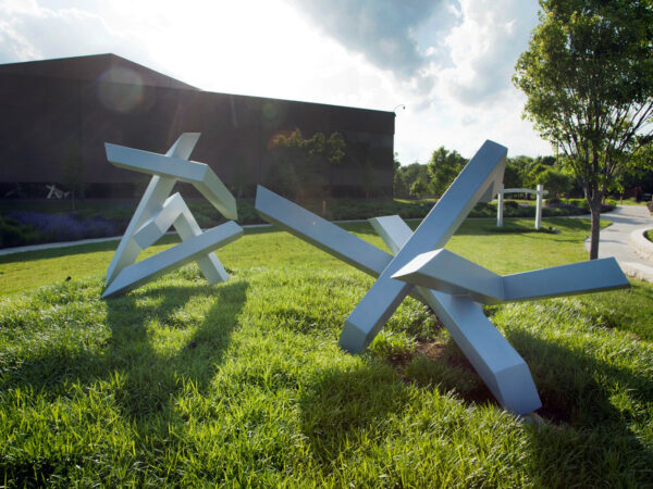 Photo of two large-scale silver abstract sculptures installed on green grass with the museum building in the background