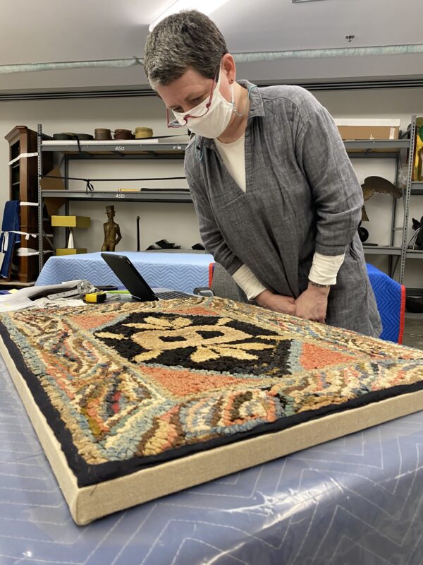 Woman wearing a mask looking down at a colorful tapestry on a table
