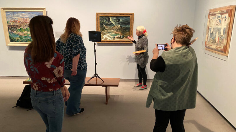 Four women in a gallery looking at art and recording a virtual tour