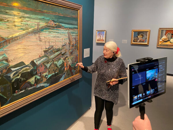 Woman in a gallery looking at a landscape painting while talking to the camera and recording a virtual tour