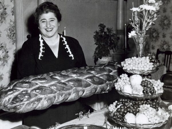 Smiling woman sitting at a table with a large challah bread