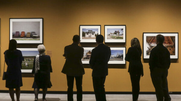 Photo of six museum vistors standing in front of a dark yellow wall looking at seven photos from the Kansas Land exhibition