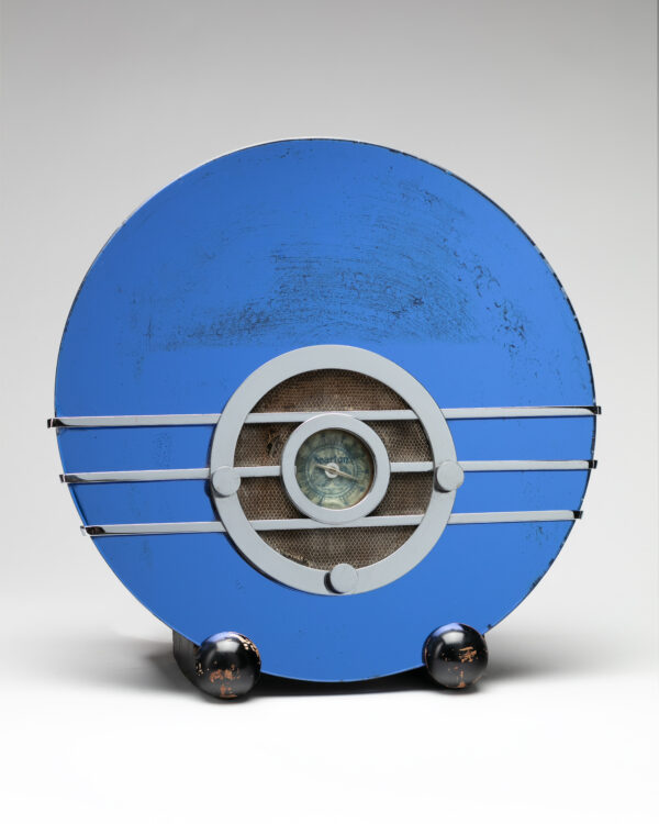 Round blue radio with silver speaker and control knobs on two shiny round black feet