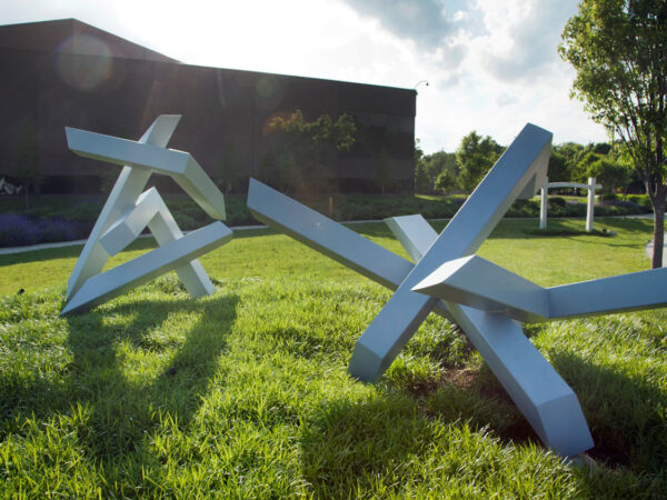 Photo of two large-scale silver abstract sculptures installed on green grass with the museum building in the background