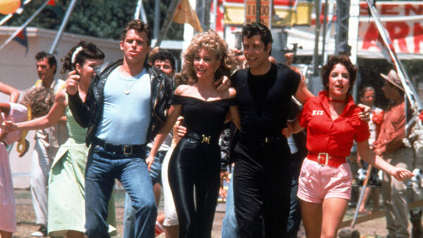 Movie still from Grease with four people walking with arms linked.