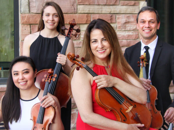 Photo of the Carpe Diem String Quartet: from left, woman with long black hair and dressed in white holding a violin. behind her is a woman with long dark hair and dressed in black, holding a cello. Center front is a woman with long, dark hair, dressed in red holding a viola. At right is a young man, dressed in the black suit jacket, white shirt and blue tile with a violin held at his right side.