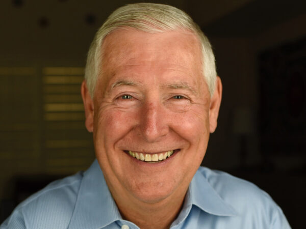 Smiling man with white hair, with a blue, collared shirt