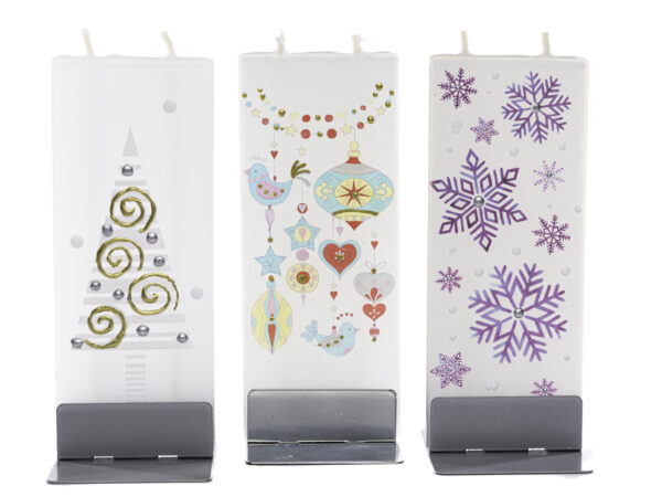 Three flat handmade candles in holiday motifs sitting in silver bases