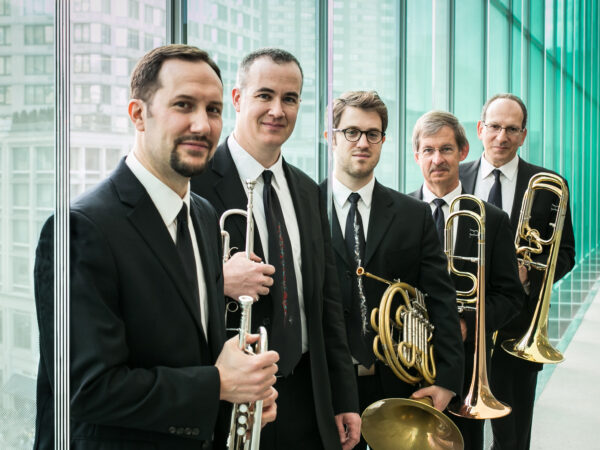 Five men dressed in dark suits, each holding a brass musical instrument