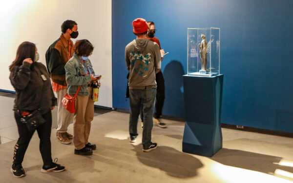People in the gallery with a sculpture on a blue pedestal.