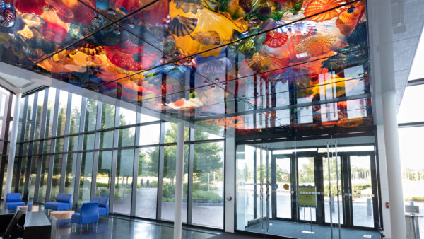 Museum's lobby with front doors, large windows, colorful glass in the ceiling and furniture in the background