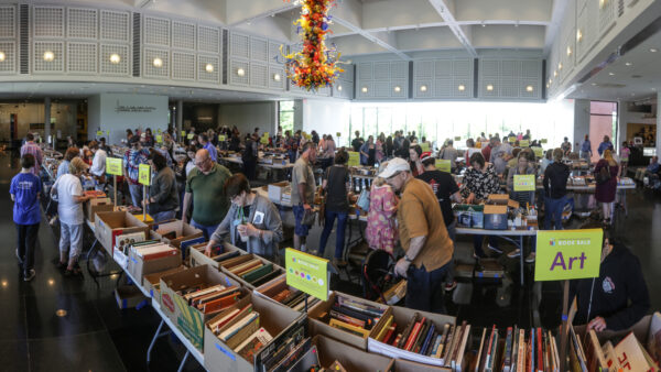 Photo of dozens of people in the S. Jim and Darla Farha Great Hall looking at hundreds of book for sale spread out over tables that fill the entire area