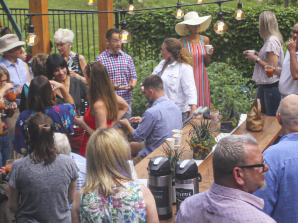 Group of 22 people at a summer party standing on a patio in a backyard with lights hanging overhead