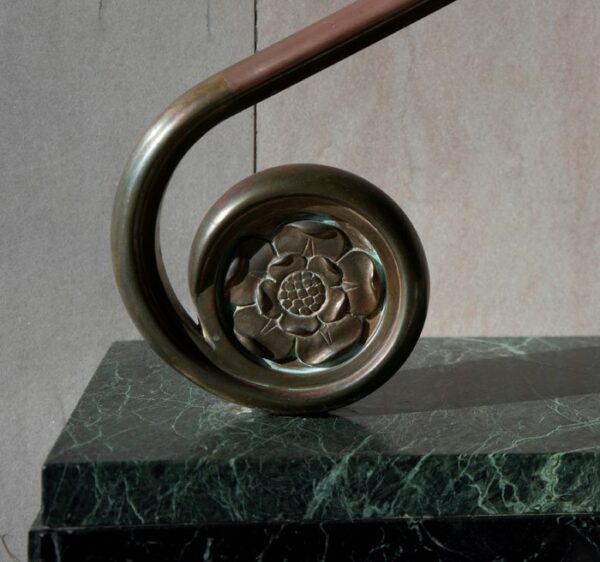 Round bronze ornament with a flower motif on a green marble base