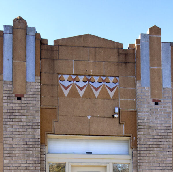 Building facade with geometric patterms in red and blue. Center pannel is red stone with an inset pattern of down-pointing arrows in blue and red, flanked by brick columns topped with red and blue pillars.
