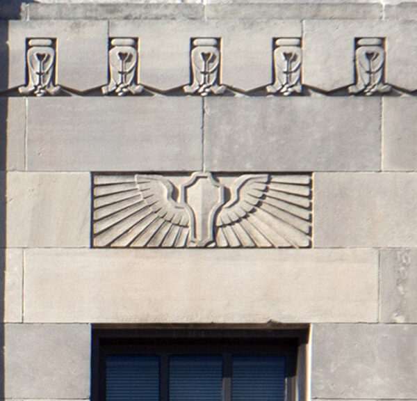 Building facade with sculpture suggestive of an eagle with outstretched wings. Above is a carved floral pattern