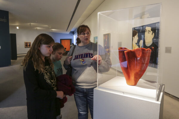 Family group of two youth and an adult in the gallery, looking at orange sculpture