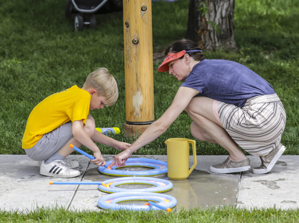 Boy in yellow shirt and kakhi shorts and woman in blue shirt and striped shorts kneeling on a sidewalk with three blue rights in front of them.