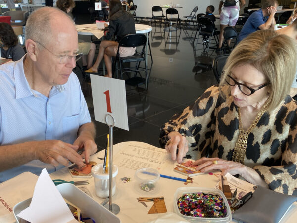 Couple sitting at a table with art supplies in front of them, decoupaging a coaster