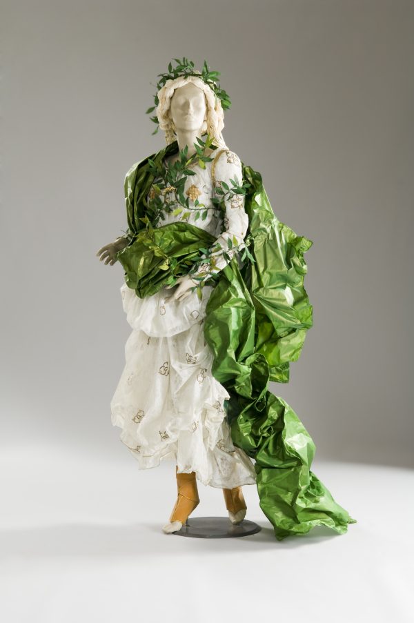 Photo of a mannequin in a dress made of paper that looks like real fabric. White dress with green motifs, with a leaf green shawl and leafy vine across the bodice.