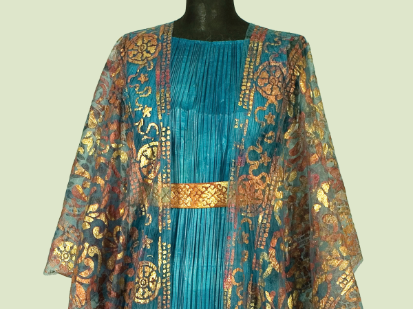 Photo of a paper dress that looks like real fabric in ruffled teal with a gold belt and a sheer gold overlay shawl with a decorative motif