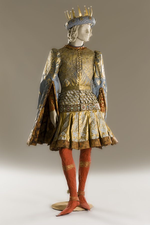 photo of a mannequin wearing a paper costume that looks like real fabric. Gold and green patterned tunic, over a gold and white skirt. Red leggings and boots