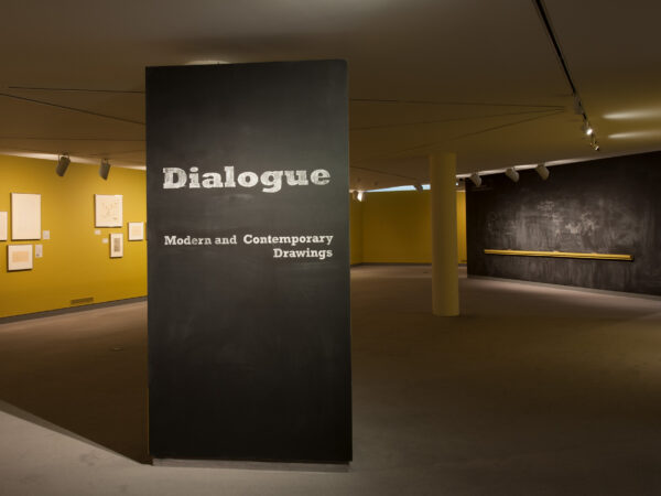 Gallery image of Dialogue with title wall in the foregound. At the left several artwork are visible. On the right, a chalkboard is visible.