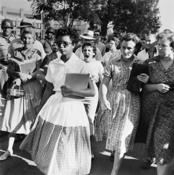 Photograph of black girl walking in front of a crowd of white women, visibly yelling at her.